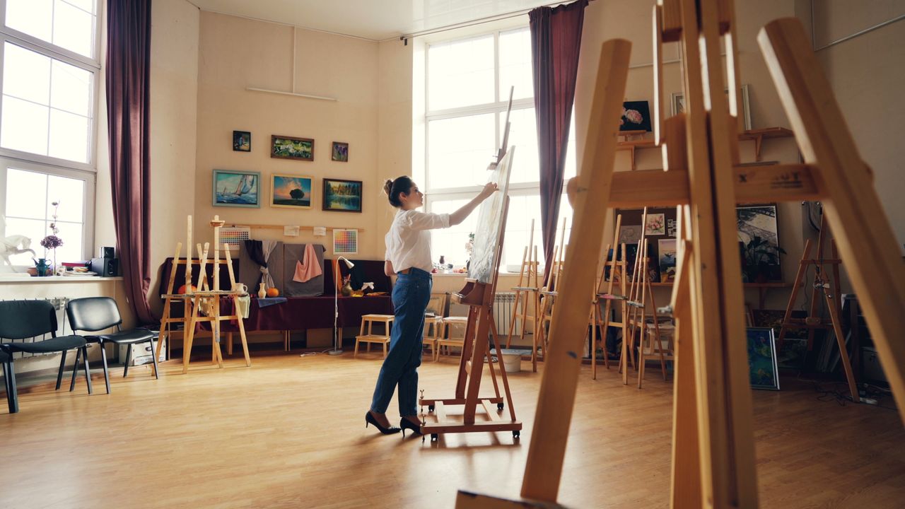 my-steps A person painting on a canvas in a sunlit art studio with wooden easels and paintings on the walls.
