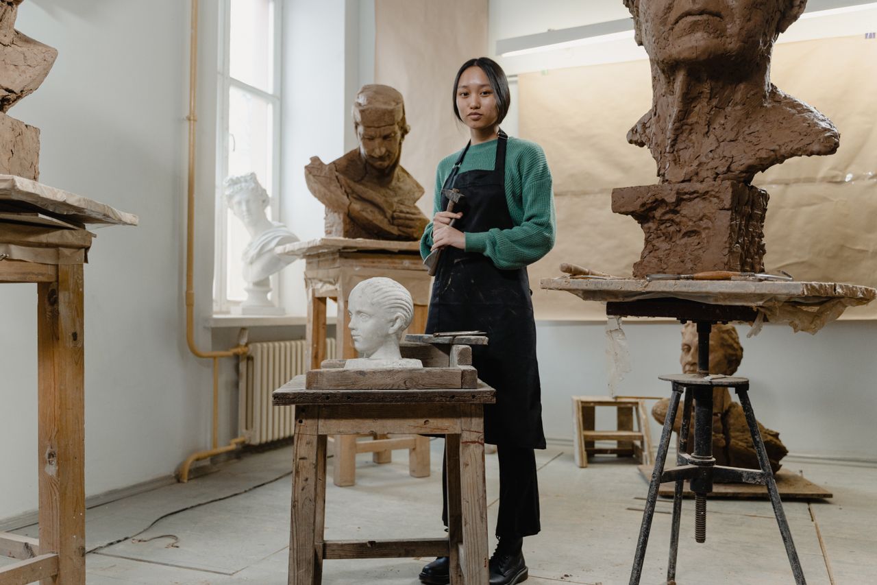 who-we-are An artist in an art studio surrounded by sculptures, showcasing creativity and skill.