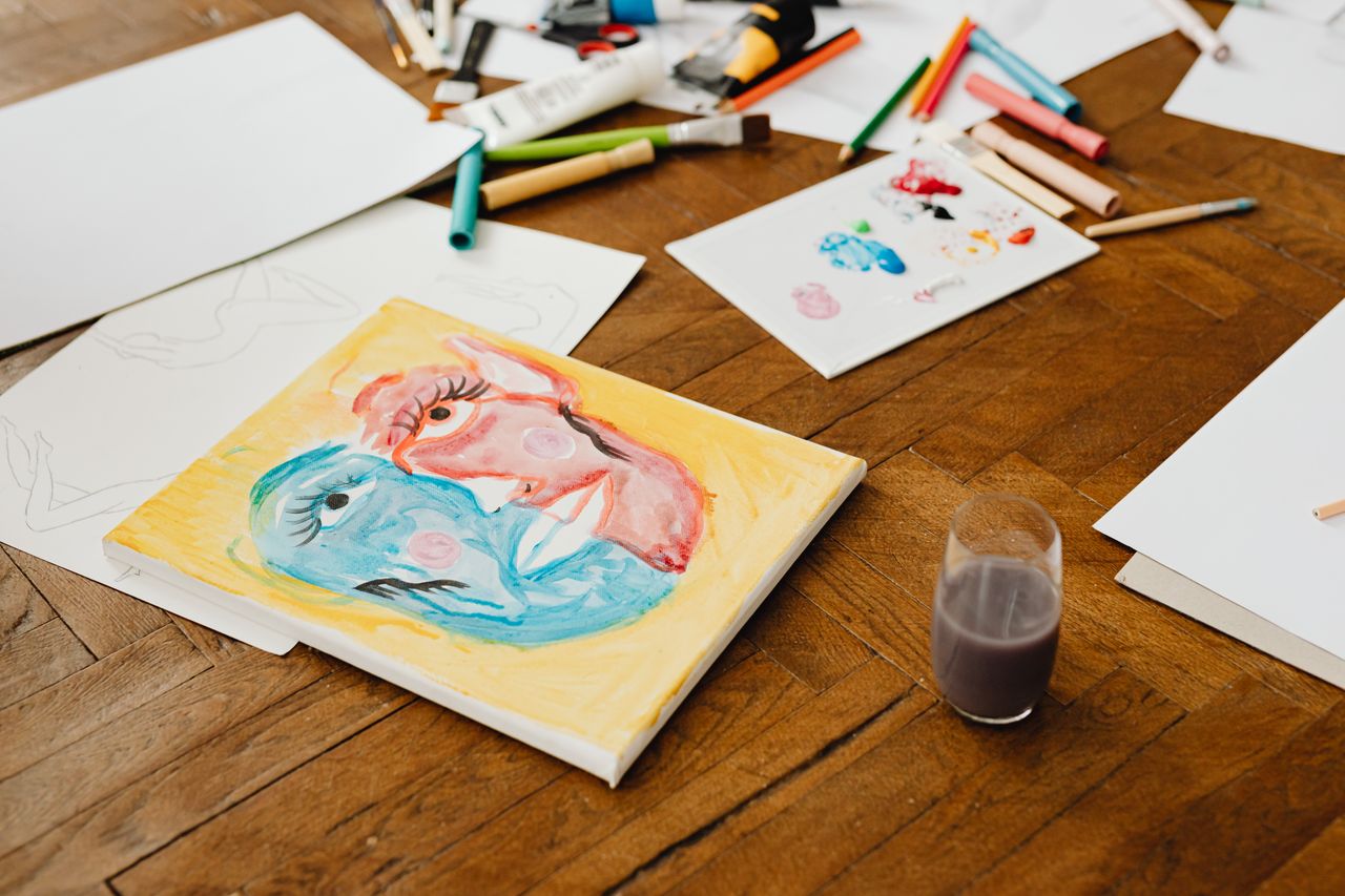 about-me-img Art supplies scattered on a wooden floor, featuring vibrant paintings and tools for creative projects.