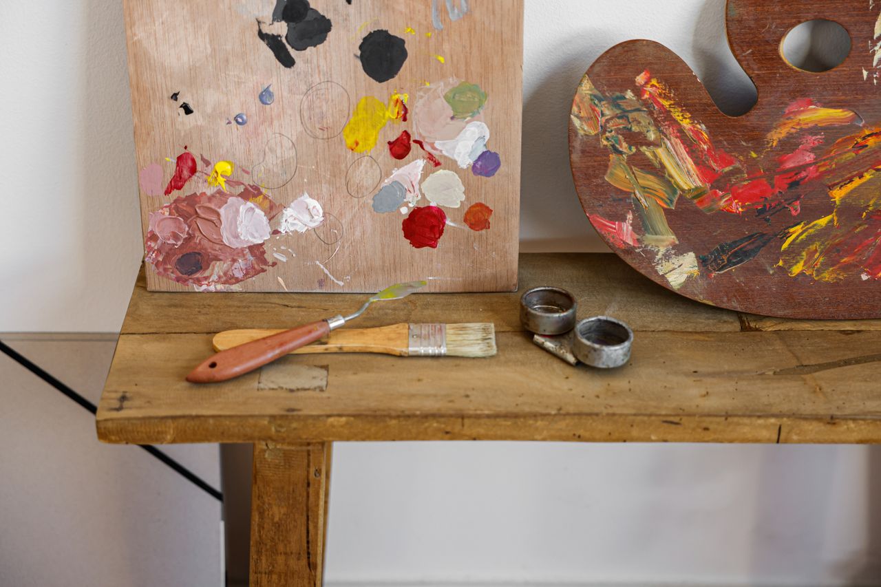 service-02 An artist's palette and brushes on a rustic wooden table, showcasing vibrant paint colors.